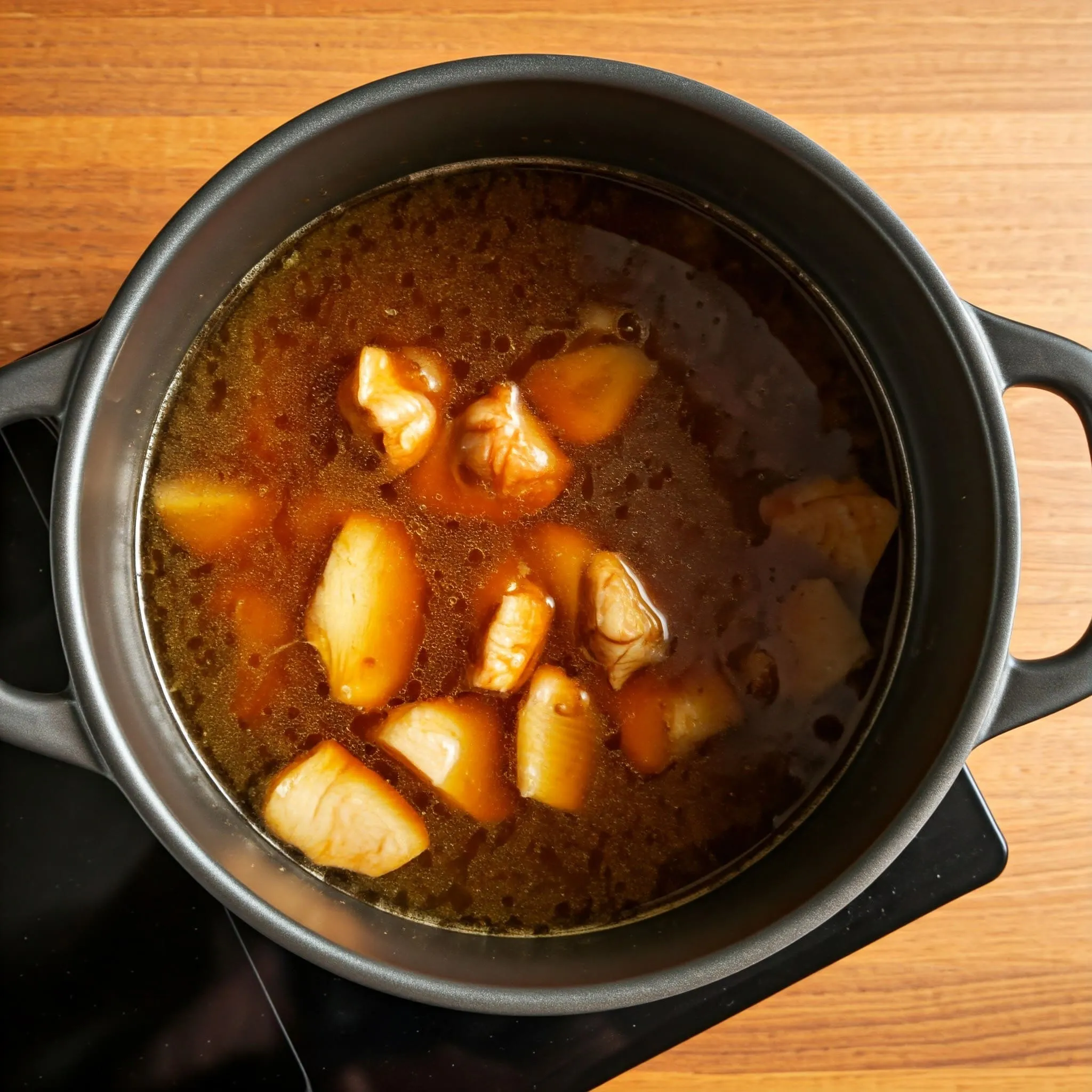 A simmering pot of chicken or pork broth with soy sauce, miso paste, ginger, and garlic, on a stovetop.