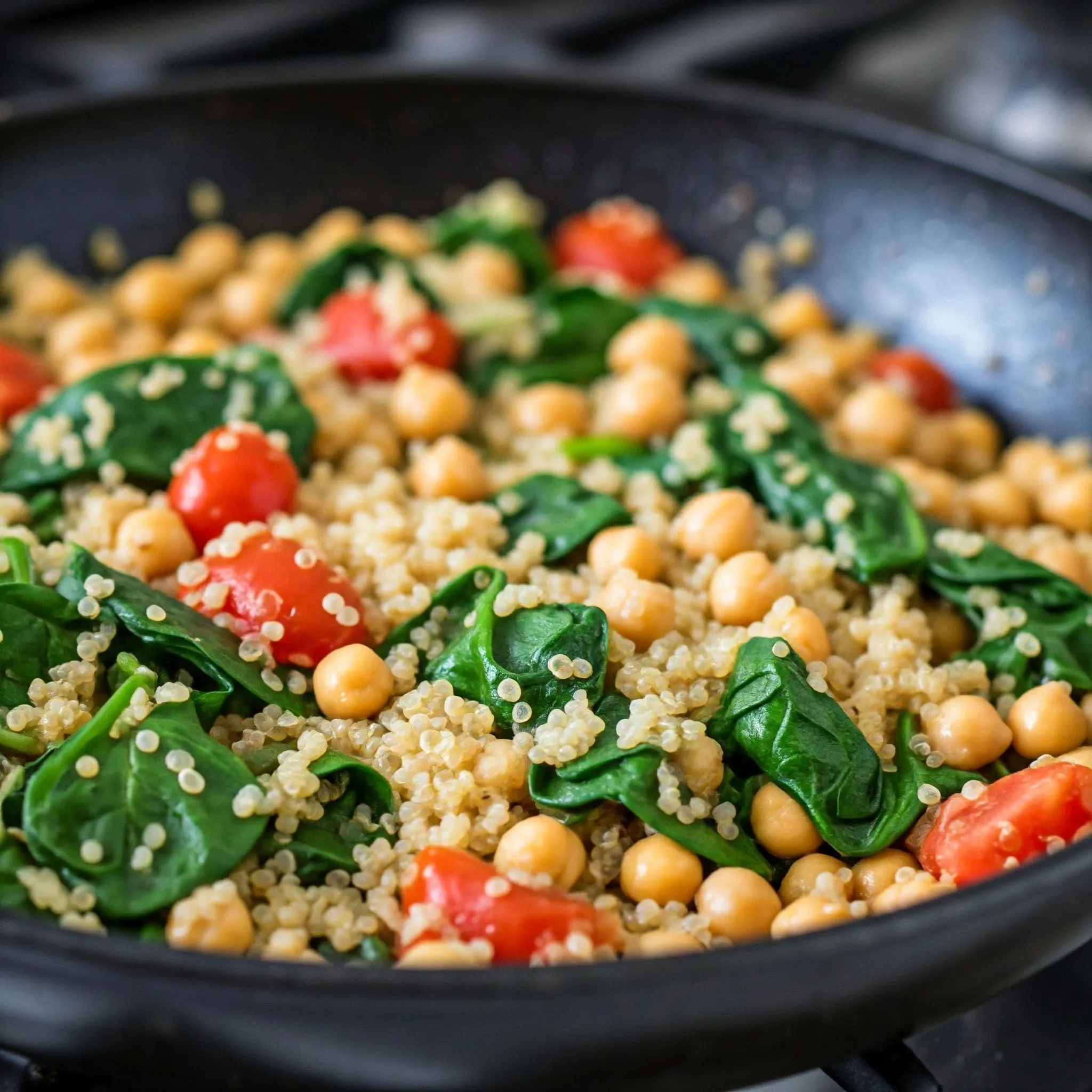 A skillet filled with quinoa, chickpeas, fresh spinach, and diced tomatoes, creating a vibrant and healthy vegetarian dish.