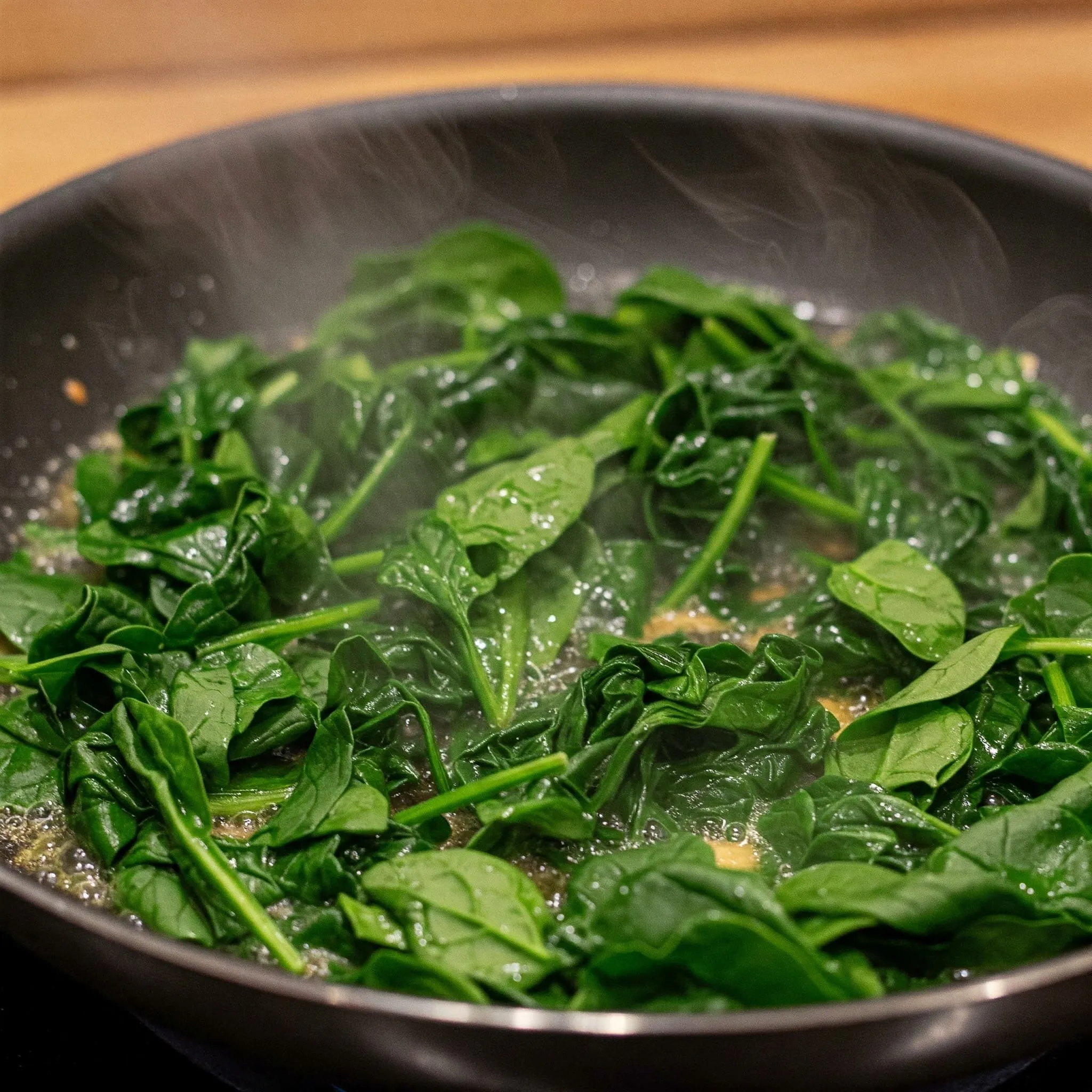 Fresh spinach wilting in a pan with butter, cooking into a tender, vibrant green.