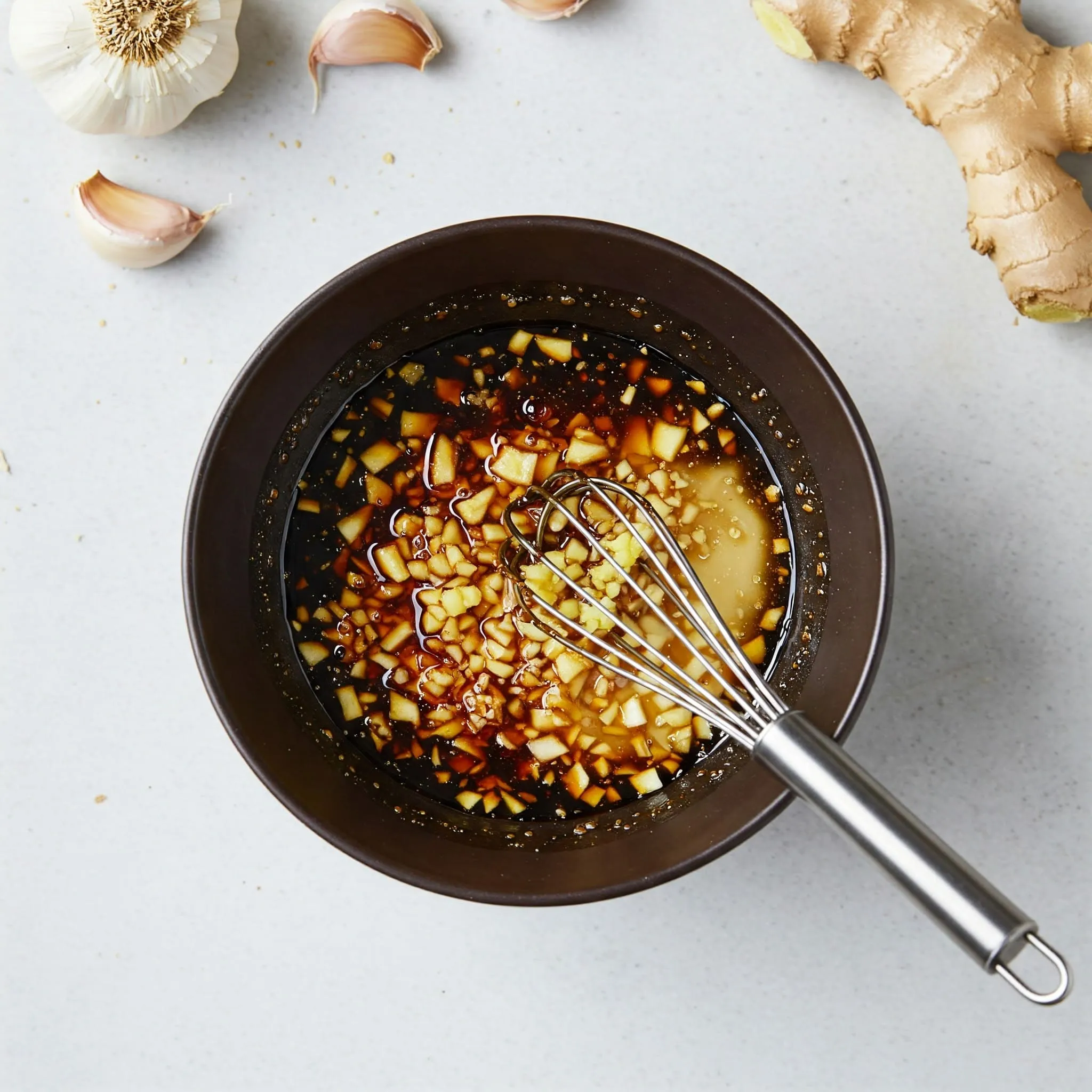 Soy sauce, rice vinegar, honey, garlic, and ginger whisked together in a small bowl for stir fry sauce preparation.