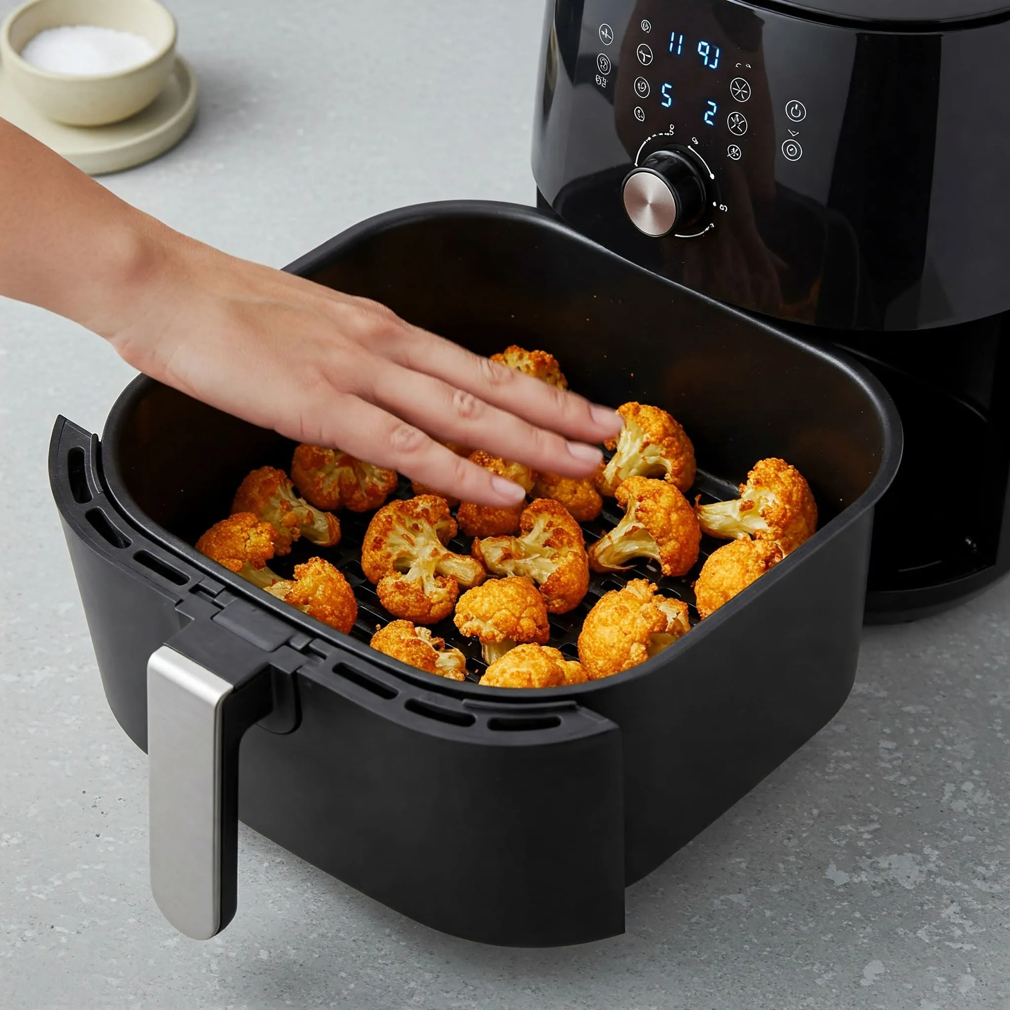 Golden, crispy cauliflower florets being cooked in an air fryer basket, with the basket being shaken halfway through for even crispiness.